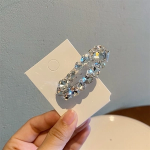 Handheld shot of an oval hair clip with sparkling clear zircons on a white display card