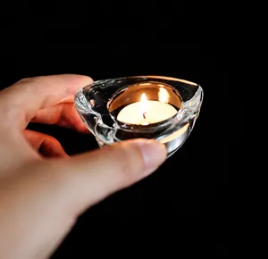 Close-up of a hand holding a heart-shaped glass candle holder with a lit tea light candle
