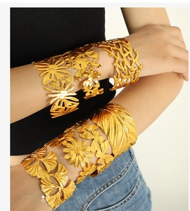 Detail of gold titanium steel arm cuffs with hollow leaf and butterfly carvings