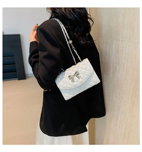 Detail of white quilted crossbody bag with silver bow buckle on elegant chain strap