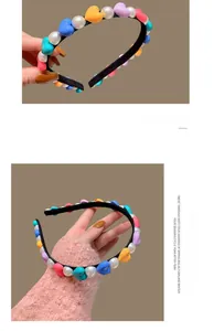Detail of a thin black headband featuring colorful hearts and white faux pearls