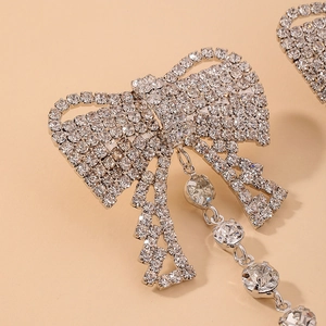 Macro shot of silver bow earrings with sparkling rhinestone fringe tassels on peach background