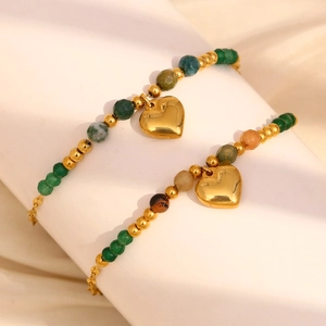 Detail of green beaded bracelets with polished gold heart charms on silk background