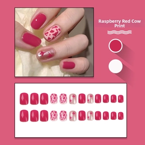Detail view of raspberry red press-on nails with cow patterns and glitter stars