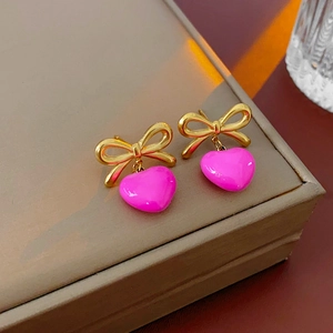 Gros plan de boucles d'oreilles nœud doré avec pendentifs cœur rose rouge sur présentoir