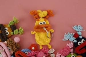 Close-up of handmade yellow knitted monster key case with orange mouth and metal ring
