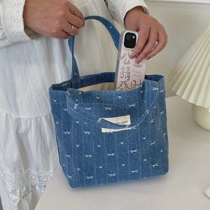Detail of blue denim tote bag with butterfly embroidery held by a model in lace dress