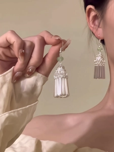 Détail de boucles d'oreilles à pompon argenté avec perle vert clair sur un mannequin