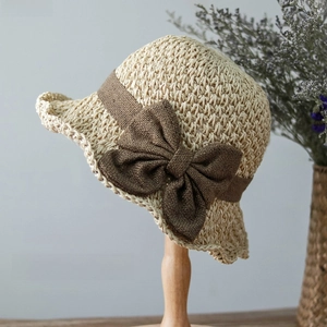 Detail of beige crochet straw cloche hat with a dark brown knit bow on a wooden stand