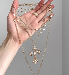 Detail of layered gold necklace featuring crystal cross and heart pendants on a hand