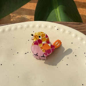 Mini acetate bird hair clip in pink and orange colors on a ceramic dish background