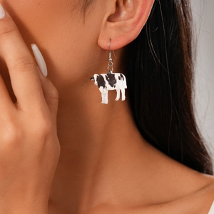 Detailed view of model wearing cow print acrylic drop earring with black and white patterns