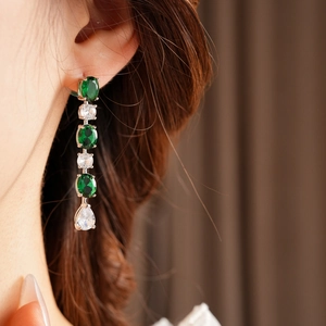 Gros plan de boucles d'oreilles pendantes en or rose avec cristaux émeraude et clairs