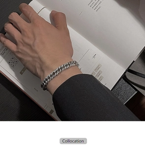 Close-up of a silver Cuban link bracelet on a man's wrist paired with a dark business suit