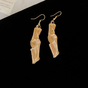 Close-up of golden irregular pleated geometric drop earrings on black velvet background