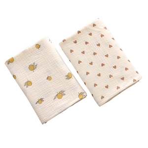 Set of two soft cotton gauze baby towels with lemon and heart patterns on white background