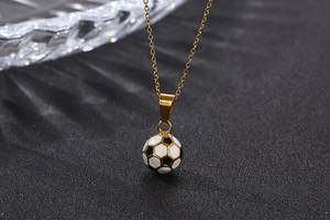 Detail of a gold-plated soccer pendant necklace on a textured black background