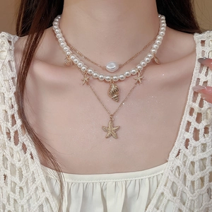 Close-up of layered necklace with starfish and conch pendants on white crochet top