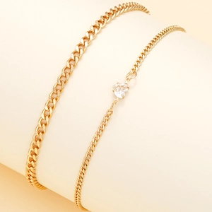 Detail showing two-piece gold stainless steel anklets with heart zircon pendant on a beige stand