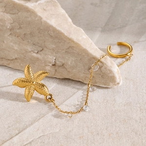 Detailed close-up of 18k gold starfish ear cuff with long crystal chain on a stone surface