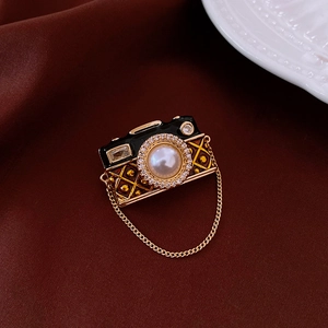 Detail of vintage camera brooch featuring a pearl lens, zircon inlay and gold chain