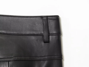 Detail view of premium black faux leather pants showing waist loops and stitching texture