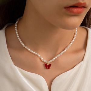 Detail of elegant pearl necklace with red butterfly pendant on a female neck