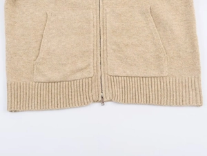 Detail of knitted hoodie showing ribbed hem, symmetric pockets and metal zipper texture