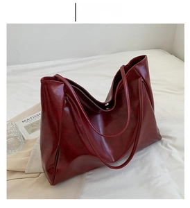 Detail view of large red oil wax leather tote bag with slender straps on white fabric