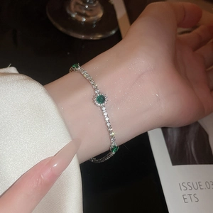 Gros plan du bracelet tennis argenté avec pierres vertes sur le poignet d'un modèle