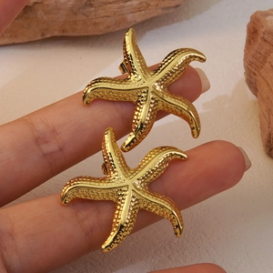 Fashionable gold starfish earrings with realistic ocean texture shown held by hand