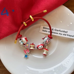 Détail d'un bracelet tressé rouge avec breloques Hello Kitty en émail sur assiette en céramique