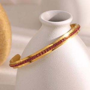 Detail of 18K gold-plated bangle with pink crystals on white ceramic bottle