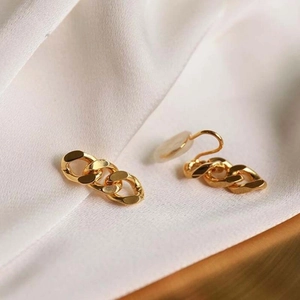 Detail of interlocking gold link earrings on white silk fabric with elegant metal luster