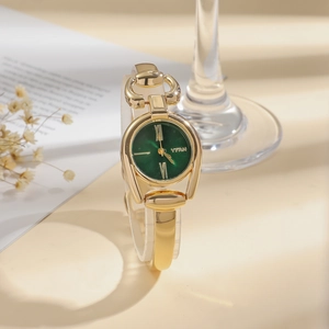 Detailed close-up of a gold bangle watch with a green dial and Roman numeral accents