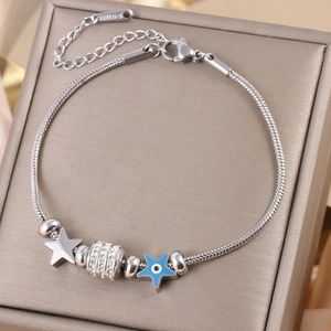 Detail of gold star and evil eye charms on a stainless steel snake chain bracelet