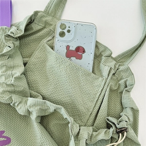 Detail of light green checkered fabric bag with ruffle trim and functional front pocket