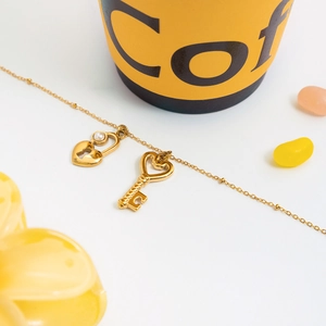 Détail du collier en acier inoxydable doré 18K avec pendentifs cadenas cœur et perle