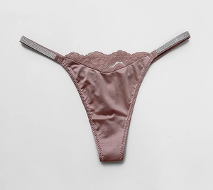 Detailed close-up of dusty pink satin thong with floral lace and rhinestone straps
