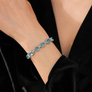 Detailed close-up of a silver bracelet with oval-cut blue cubic zirconia on woman's wrist