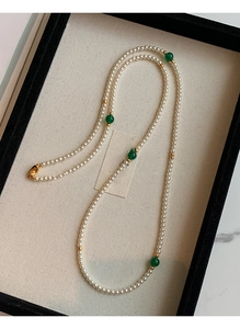 Close-up of pearl necklace with green beads and gold accents in a jewelry tray