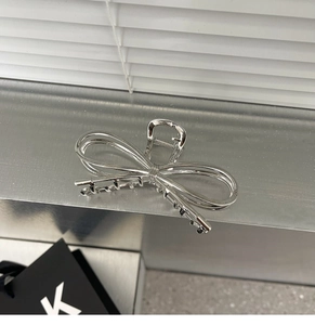 Close-up of a silver metal bow hair claw clip with polished finish on a sleek surface