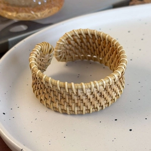 Close-up detail of a handmade woven rattan open bangle showing natural texture on a ceramic plate