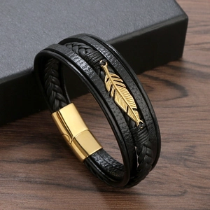 Men's woven leather bracelet with golden feather charm and magnetic clasp on wooden desk