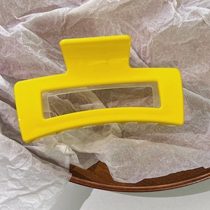 Macro shot of large yellow geometric hair claw clip on wooden tray with white paper