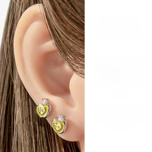 Detailansicht eines Herzohrrings mit gelber Emaille und Augendesign am Ohr eines Models