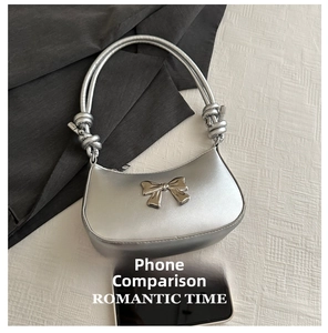Close-up of silver crescent handbag with metallic bow and knotted handle next to a phone