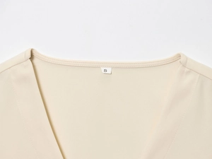 Gros plan du haut sans manches beige avec col en V, coutures nettes et étiquette taille S