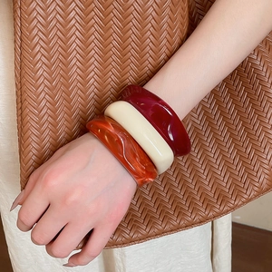 Close-up of three thick acrylic bangles in red, cream, and marble orange on a wrist