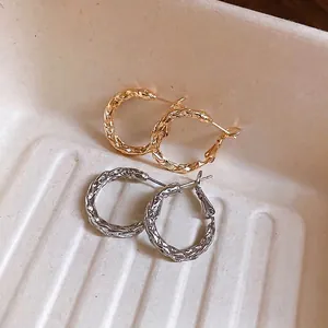 Elegant twisted rope hoop earrings in gold and silver finish on a textured background